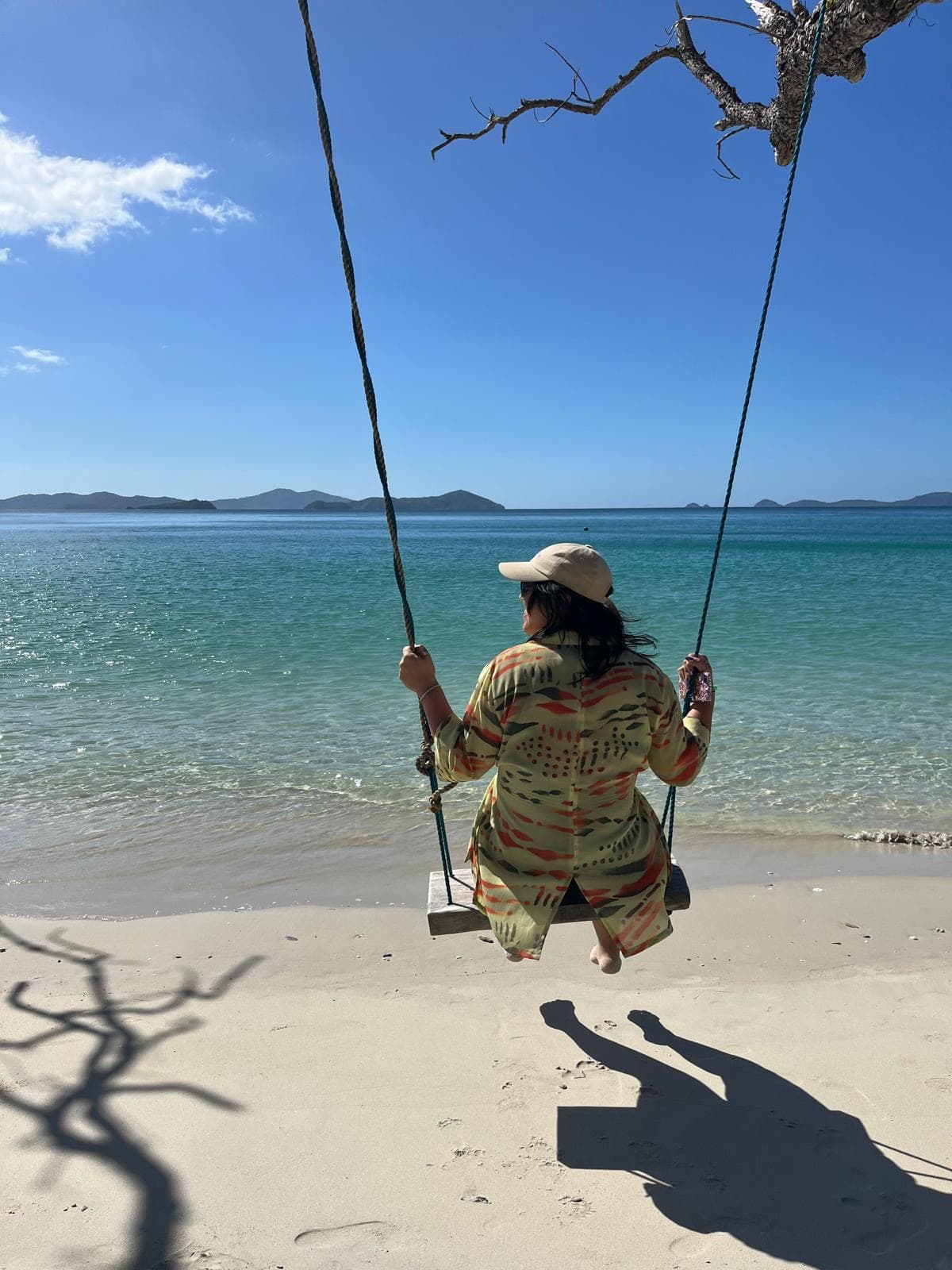 Person auf einer Schaukel am tropischen Strand mit Blick auf türkisfarbenes Meer