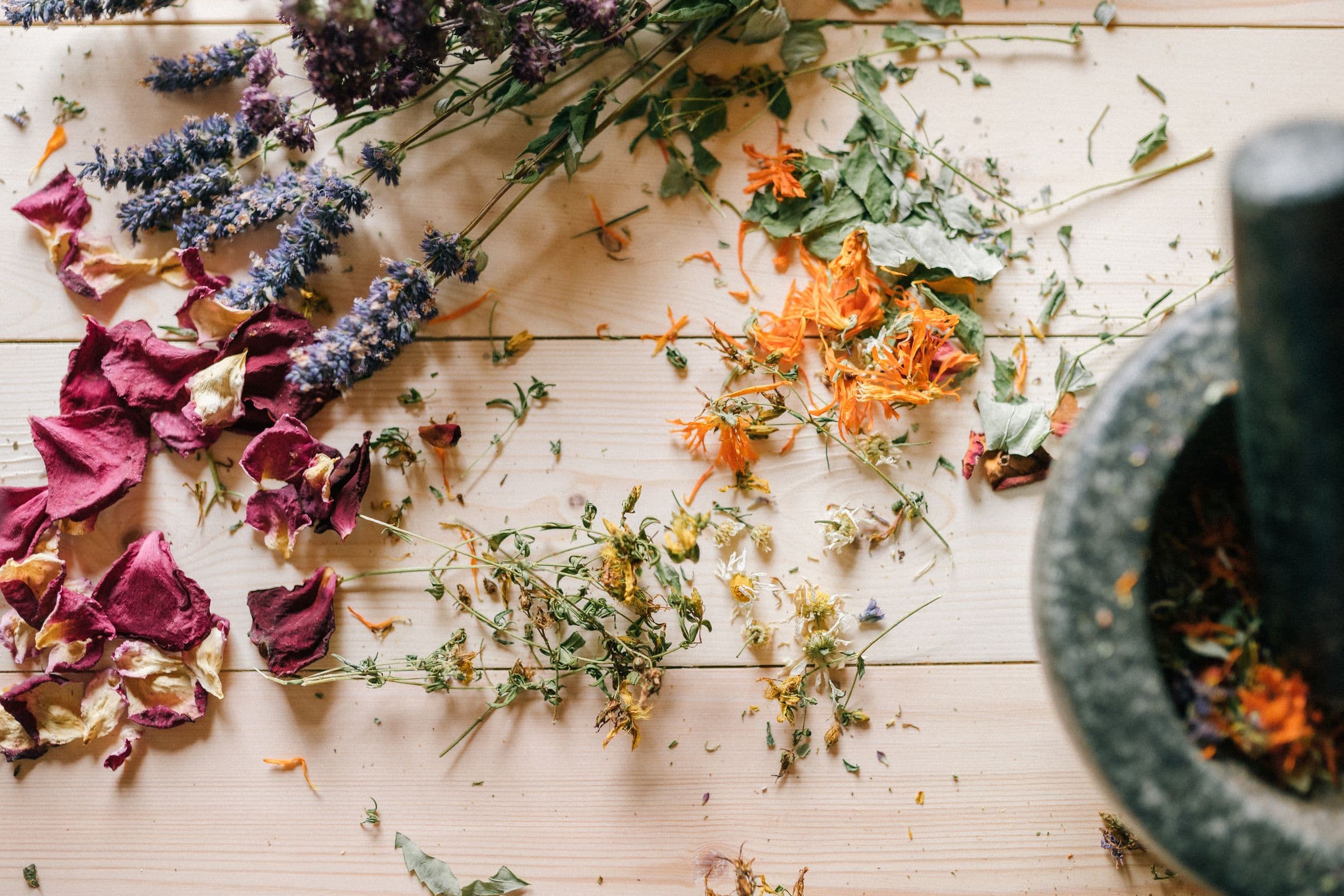 Getrocknete Kräuter, Lavendel, Rosenblätter und Ringelblumen mit Mörser auf hellem Holztisch