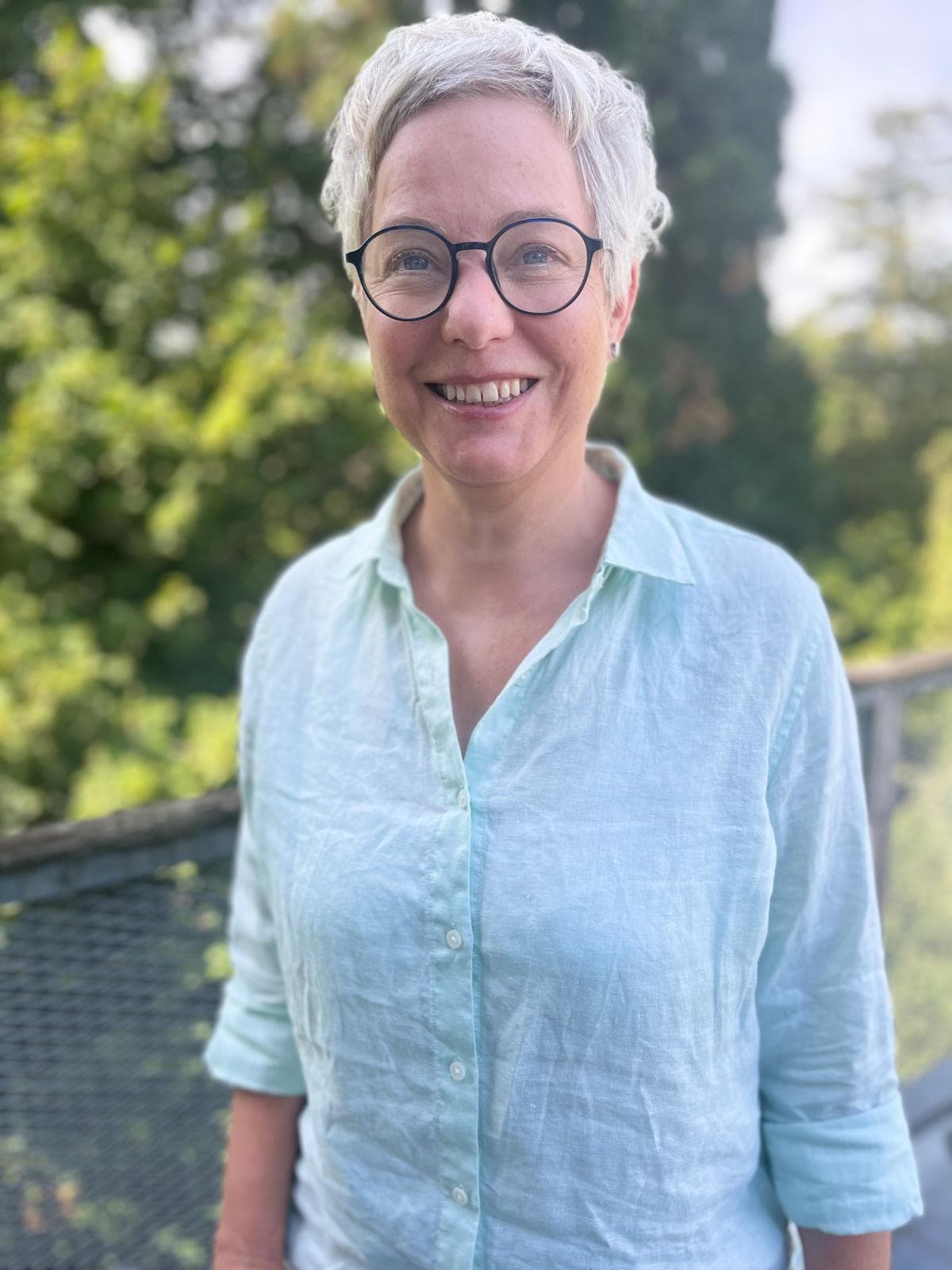 Katharina Hannesschläger in hellblauer Leinenbluse, lächelnd auf einer Terrasse im Grünen
